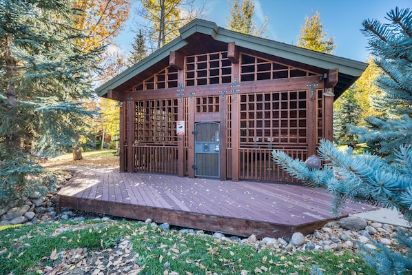 Una cabaña de madera con un porche, rodeada de árboles y rocas.