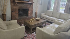 Ein Wohnzimmer mit Kamin aus Ziegelsteinen, einem darüber montierten Fernseher, einem beigefarbenen Sofa und einem Couchtisch mit Dekoration.