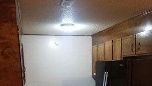 Eine Küche mit Holzausstattung, einem schwarzen Kühlschrank, einer Spüle und einem Mülleimer.