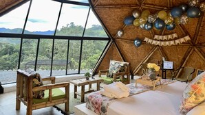 A spacious, naturally lit room with a large bed, wooden furniture, and a view of lush greenery and mountains. - Ecofuratena Glamping (Utica)