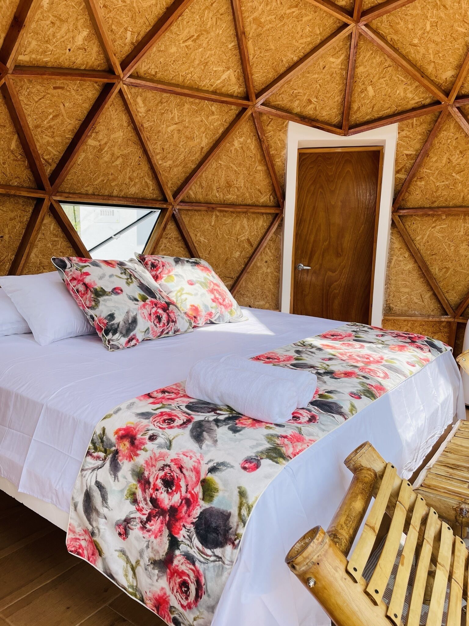 A cozy room with a bed, floral bedding, a wooden door, and a geometric ceiling design.