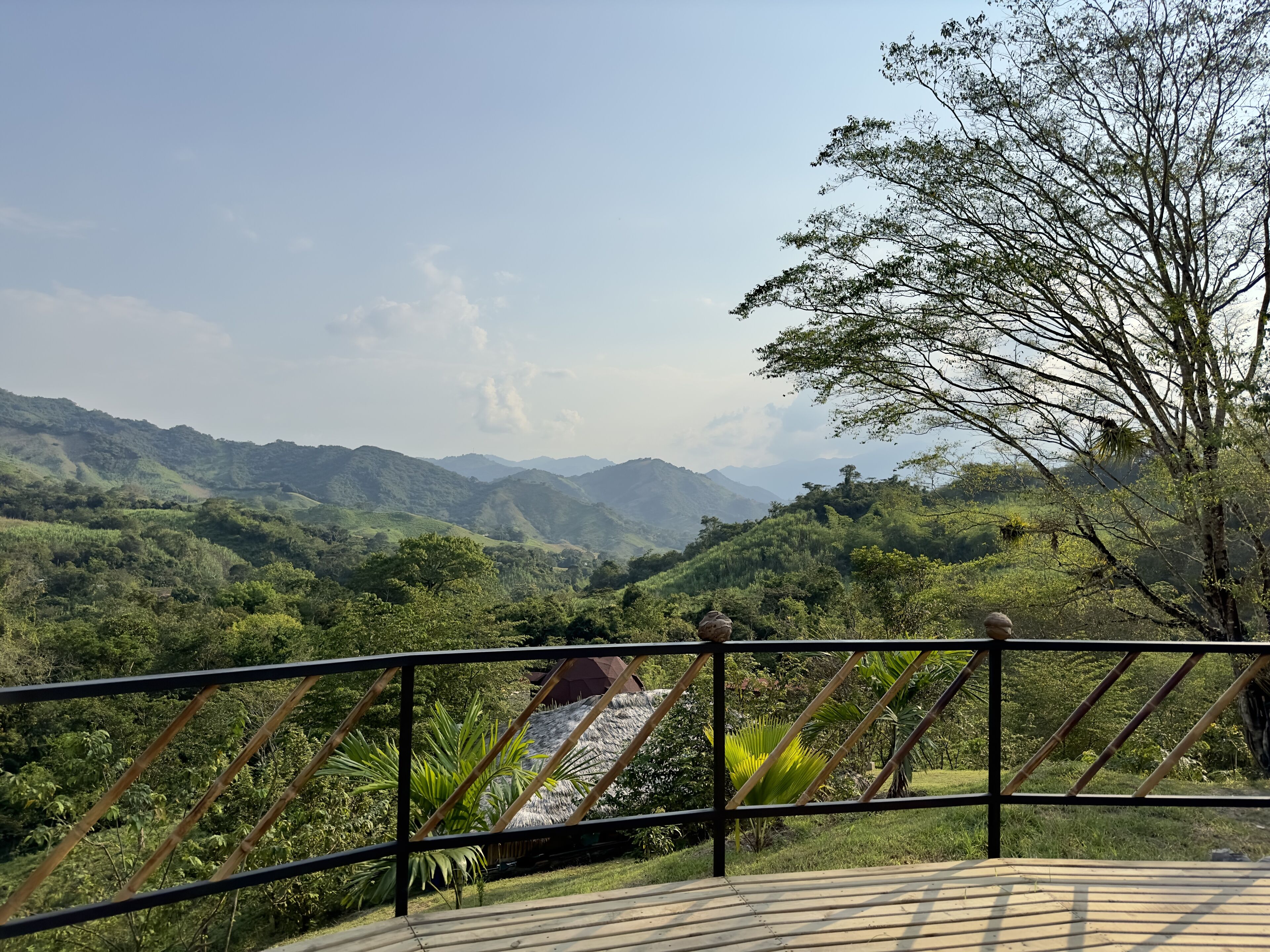 Vista panorâmica de uma varanda com guarda-corrimão de metal, mostrando colinas verdejantes e montanhas ao longe.