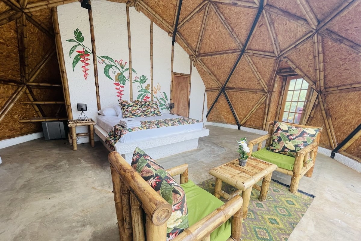 Een kamer met een bed, twee houten stoelen, een kleine tafel en een decoratieve wand.