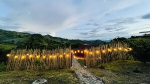 A pathway leading to a building with a red roof, surrounded by bamboo fencing and string lights. - Ecofuratena Glamping (Utica)
