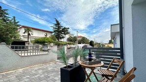 A balcony with a wooden chair, a small table, and a bottle of wine. There is a potted plant and a view of a street with houses and cars. - Studio with terrace and air conditioning (Dramalj)