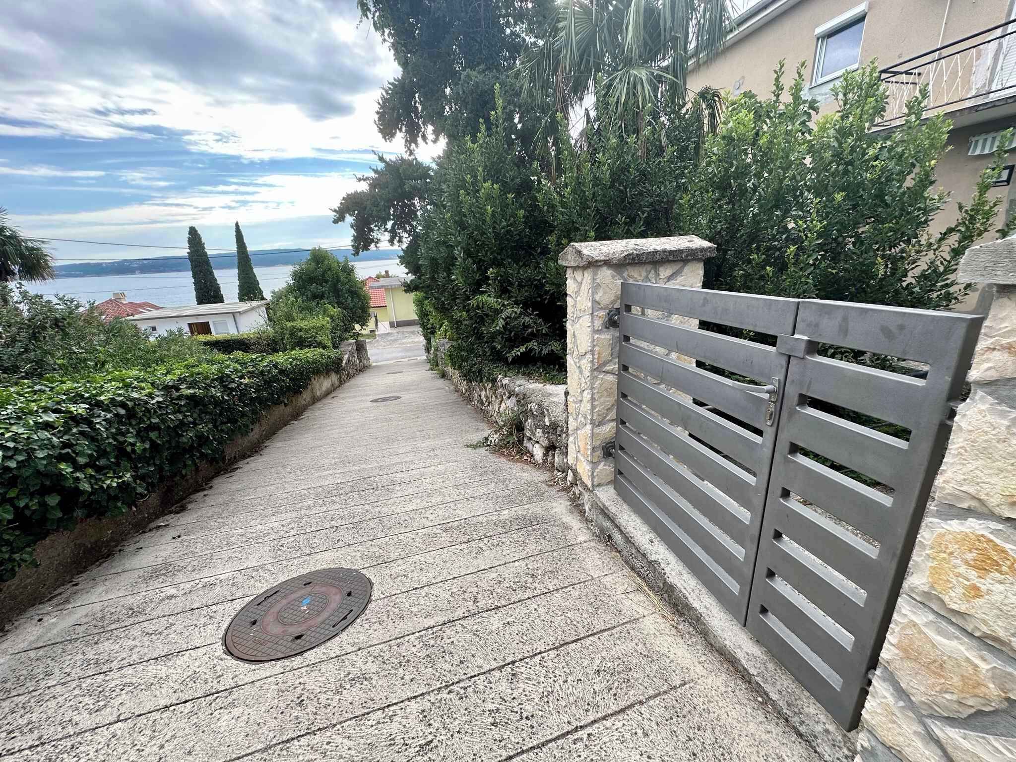 A paved pathway leading to a gated entrance with a stone wall and metal gate.