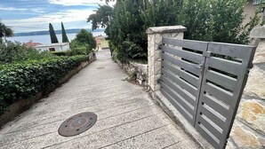 A paved pathway leading to a gated entrance with a stone wall and metal gate. - Studio with terrace and air conditioning (Dramalj)