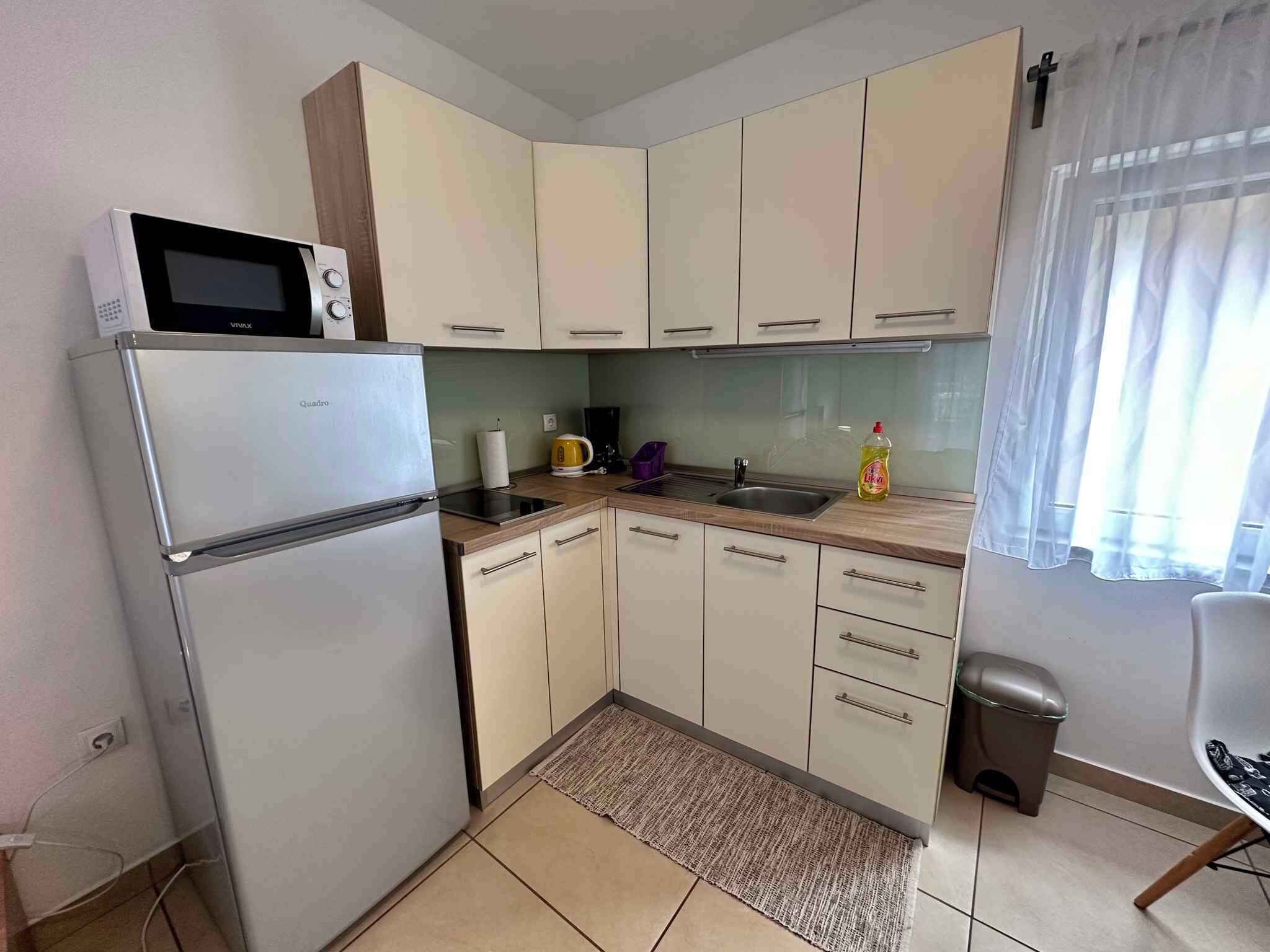 Eine kleine Küche mit Kühlschrank, Mikrowelle, Spüle und Schränken.