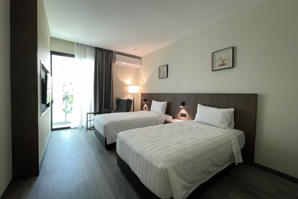 Ein Hotelzimmer mit zwei Betten, einem Schreibtisch, einem Stuhl, einer Lampe und einem Fenster mit Vorhängen.