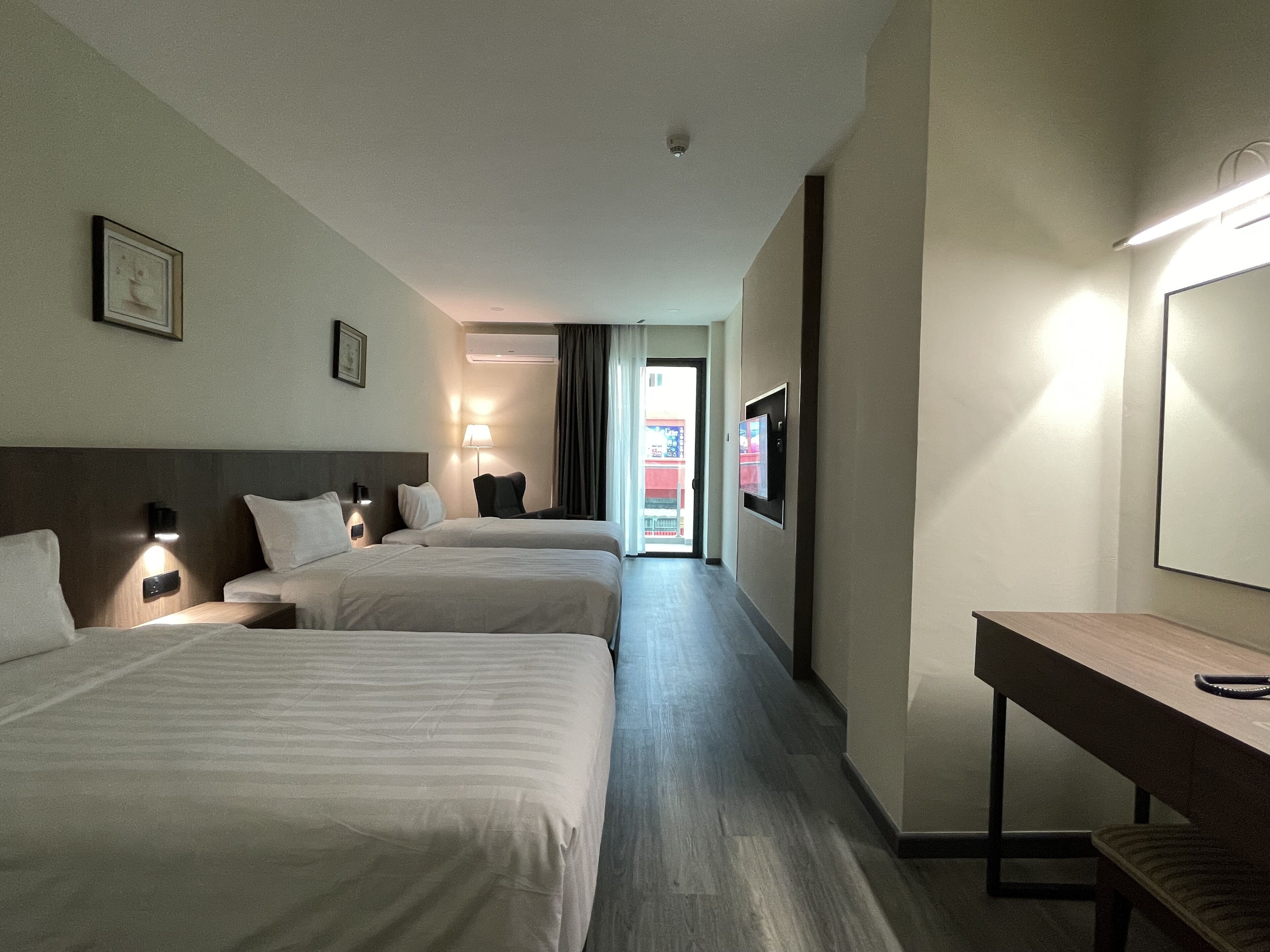 A hotel room with two beds, a desk, a TV, and a window with curtains.