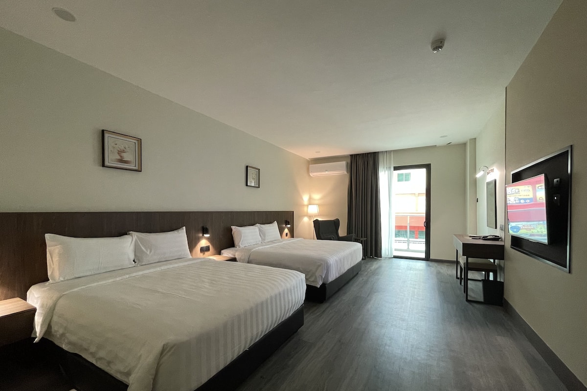 Ein Hotelzimmer mit zwei Betten, einem Schreibtisch, einem Stuhl, einem Fernseher und einem großen Fenster.
