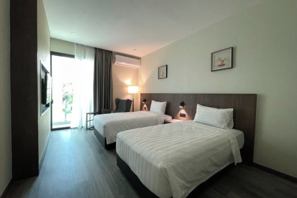 A hotel room with two beds, a desk, a chair, a lamp, and a picture on the wall.