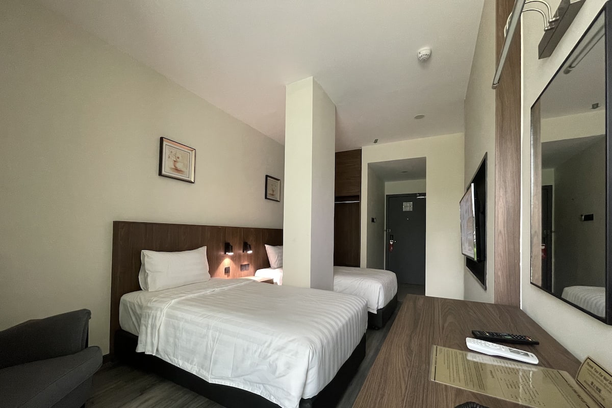 Ein Hotelzimmer mit einem großen Bett, einem Schreibtisch mit Stuhl, einer Couch, einem Fernseher und einem Spiegel.