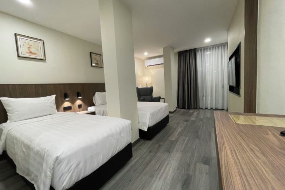 A hotel room with two beds, a desk, a chair, a TV, and a window with curtains.