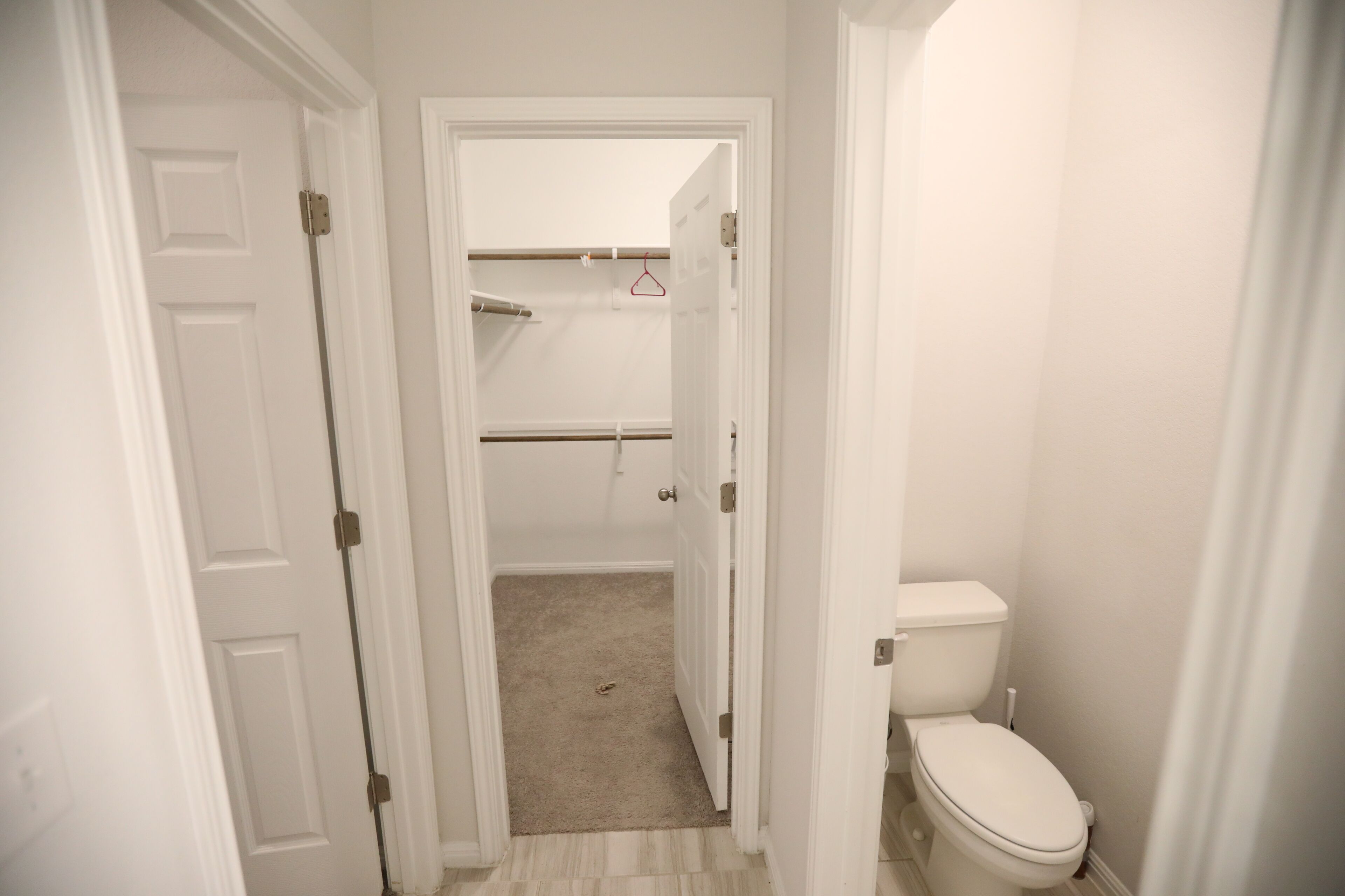 A narrow hallway leading to a bathroom with a toilet and a closet.