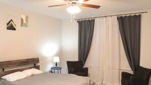A bedroom with a bed, two chairs, a nightstand, a lamp, and a ceiling fan. - Family and group friendly large, spacious modern home in Leander (Andice)