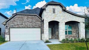 A two-story house with a stone facade, a garage, and a well-maintained lawn. - Family and group friendly large, spacious modern home in Leander (Andice)