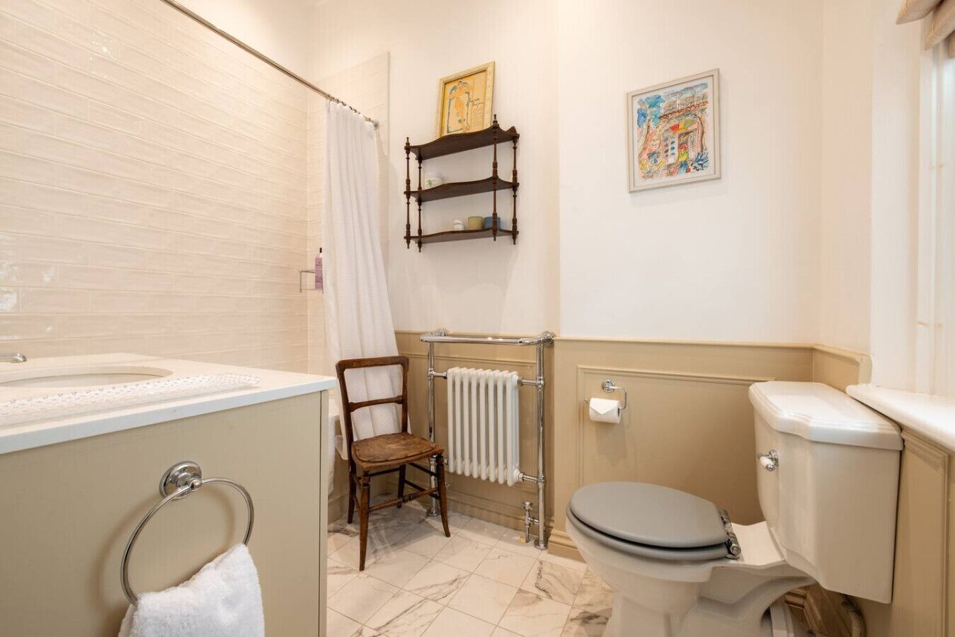 Une salle de bain comprenant des toilettes, un lavabo, une chaise, un radiateur et deux tableaux encadrés accrochés au mur.