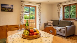 A cozy living room with a wooden table, a bowl of fruit, a sofa, and a window with curtains.