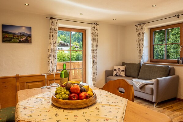 A cozy living room with a wooden table, a bowl of fruit, a sofa, and a window with curtains.