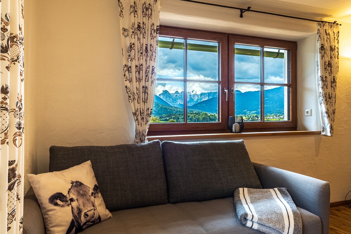 A room with a sofa, a window with a mountain view, and patterned curtains.