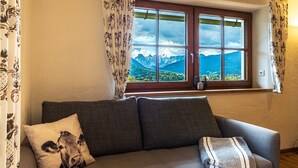 A room with a sofa, a window with a mountain view, and patterned curtains.