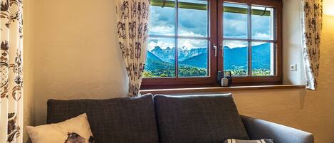 A room with a sofa, a window with a mountain view, and patterned curtains.