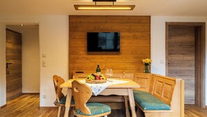 Een eetruimte met een houten tafel, banken en een aan de muur bevestigde televisie.