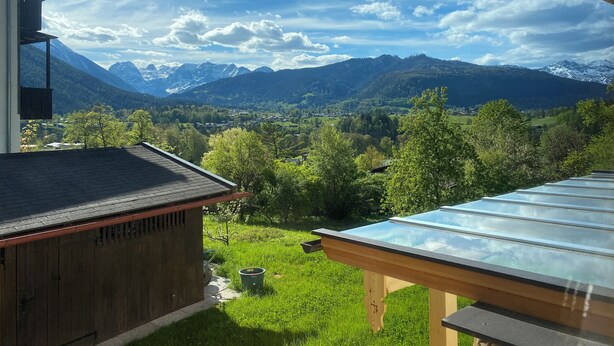 Uitzicht vanuit een kamer met een glazen tafel en houten constructie, met zicht op een vallei met bergen en een heldere lucht.
