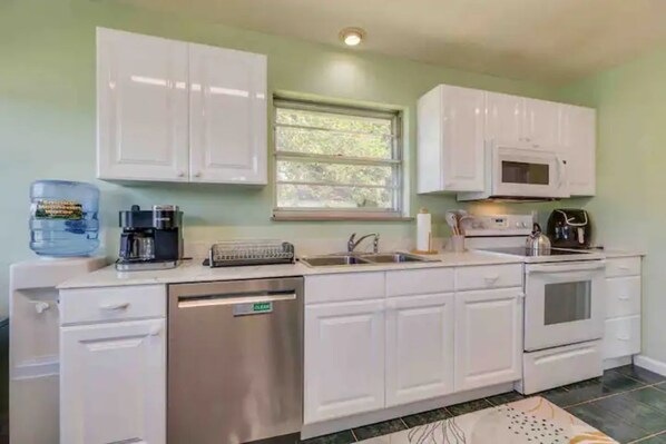 A compact kitchen with white cabinets, a built-in microwave, a dishwasher, and a window with a view of greenery.