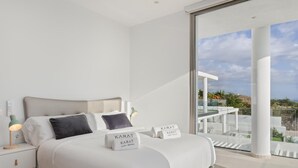 Une chambre moderne avec un grand lit, des lampes de chevet et une vue sur un balcon aménagé avec du mobilier d’extérieur.