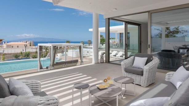 Un espace de vie extérieur moderne doté d’une piscine, de chaises longues et d’un patio fermé par des parois de verre.