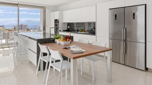 Une cuisine moderne avec des meubles blancs, un réfrigérateur en acier inoxydable et un coin repas avec des chaises blanches.