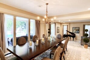 Formal dining area with a long table, chandelier, and grand piano.