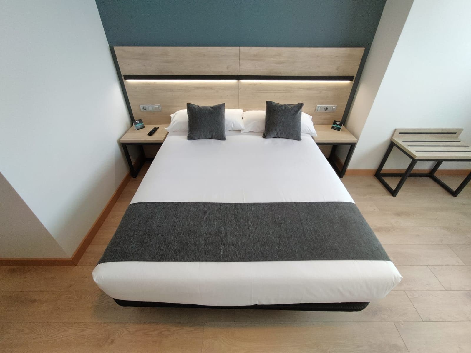 Una habitación de hotel con una cama grande, dos mesitas de noche y un pequeño banco de madera.