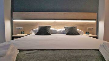 A neatly made bed with a headboard, two pillows, and a remote control on a bedside table.