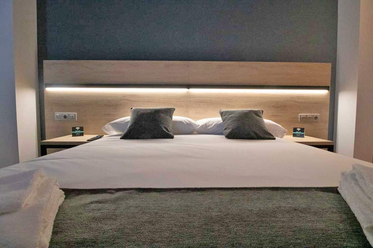 Cama bem arrumada com cabeceira, dois travesseiros e um controle remoto sobre a mesa de cabeceira.