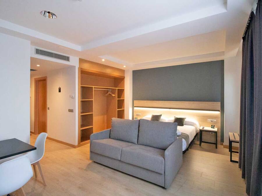 A modern hotel room with a sofa, a bedside table, a wardrobe, and a large bed.