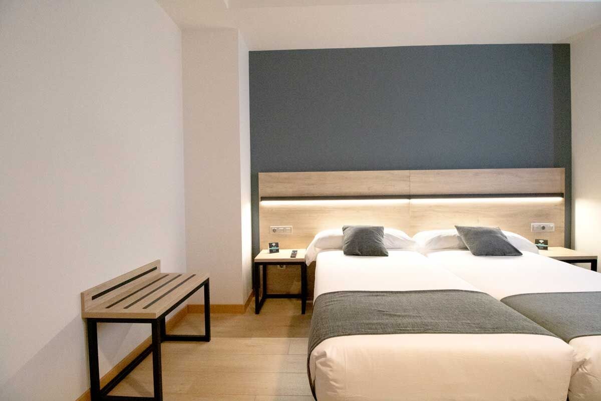 A hotel room with a bed, bedside tables, a bench, and a headboard.
