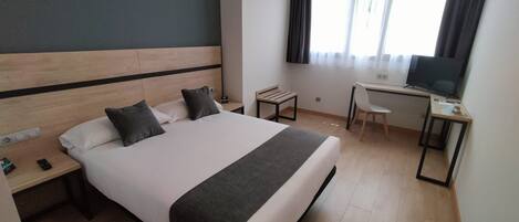 Habitación de hotel con una cama grande, un escritorio con silla, televisor y ventana con cortinas.
