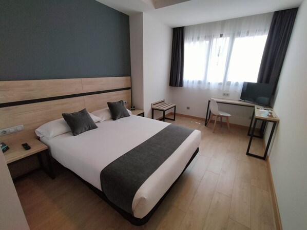 Une chambre d’hôtel avec un grand lit, un bureau avec une chaise, une télévision et une fenêtre avec des rideaux.