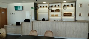 A hotel reception area with a wooden reception desk, a television mounted above it, and a wall with shelves displaying wicker baskets and potted plants.