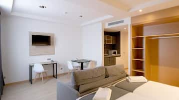 A modern hotel room with a sofa bed, a desk, a flat-screen TV mounted on the wall, and a walk-in closet.