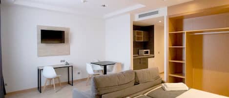 Una habitación de hotel moderna con sofá cama, escritorio, televisor de pantalla plana montado en la pared y vestidor.