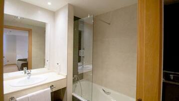 A modern bathroom with a large mirror, a white sink, a glass-enclosed shower, and a wooden door.