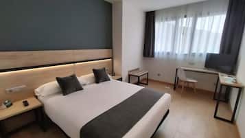 A hotel room with a bed, bedside tables, a desk, a chair, and a TV.