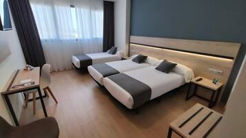 Quarto de hotel com duas camas, uma escrivaninha, uma cadeira e uma mesinha.