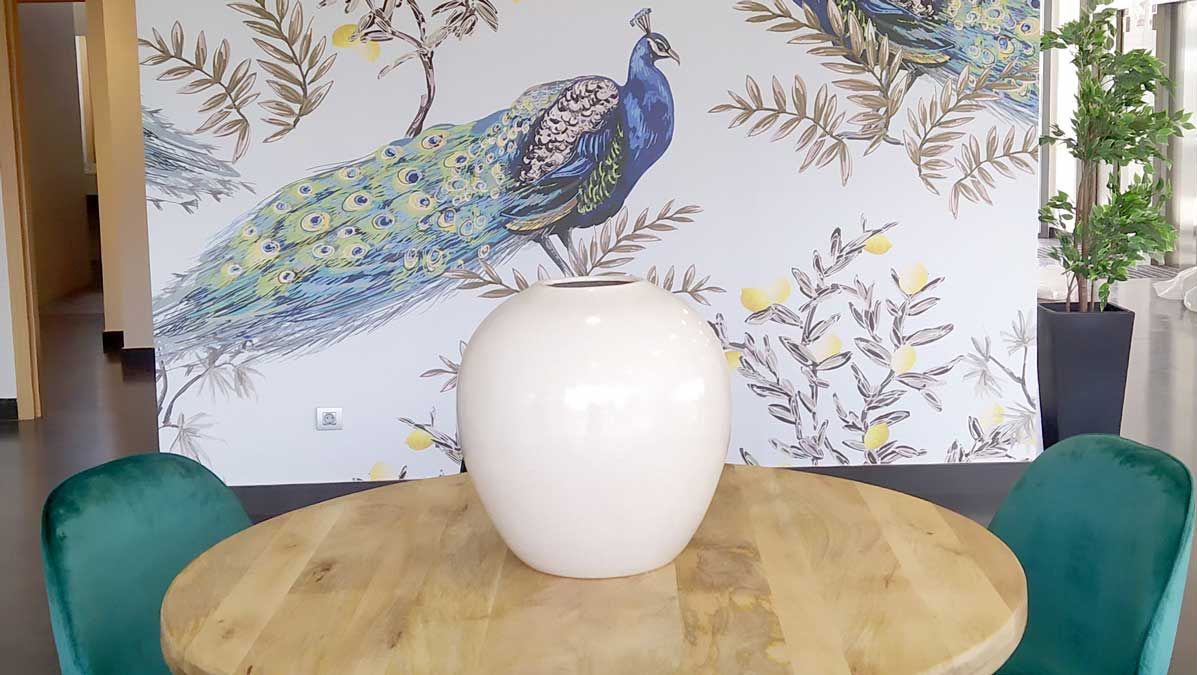 A dining area with a round wooden table, a white vase, and teal chairs.