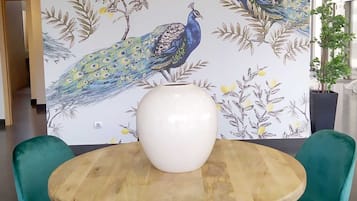 A dining area with a round wooden table, a white vase, and teal chairs.