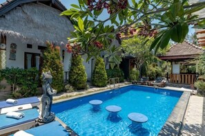 A swimming pool with lounge chairs and a statue, surrounded by greenery and a thatched-roof building. - The Kubon Beach by ABM (Bali)